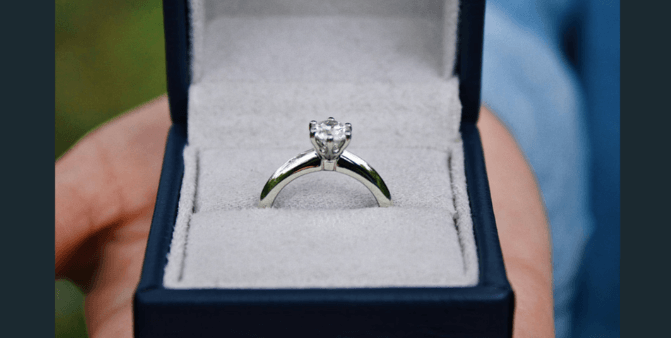 Hand holding engagement ring in a box